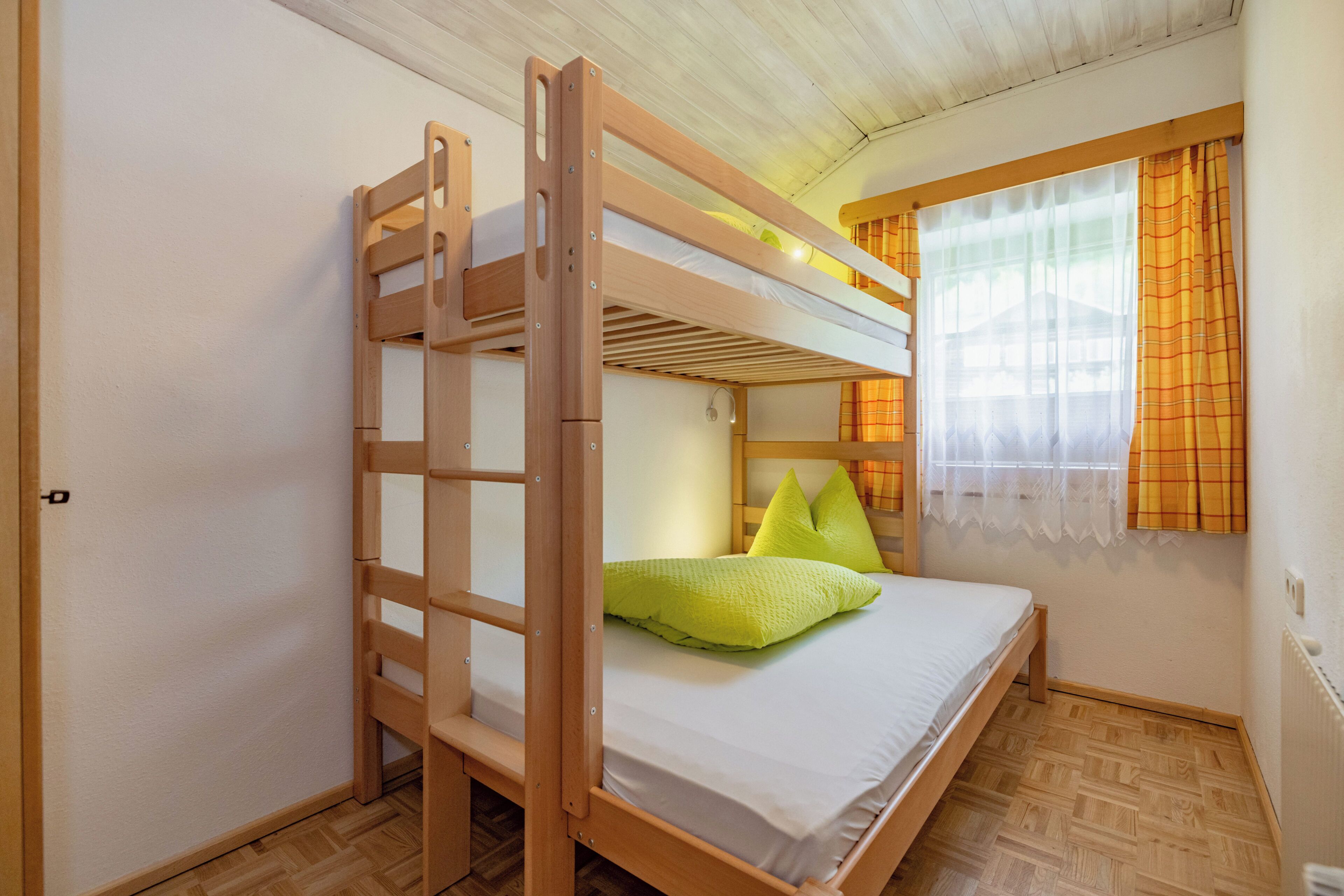 A bunk bed with a ladder, a window with curtains, and a radiator.