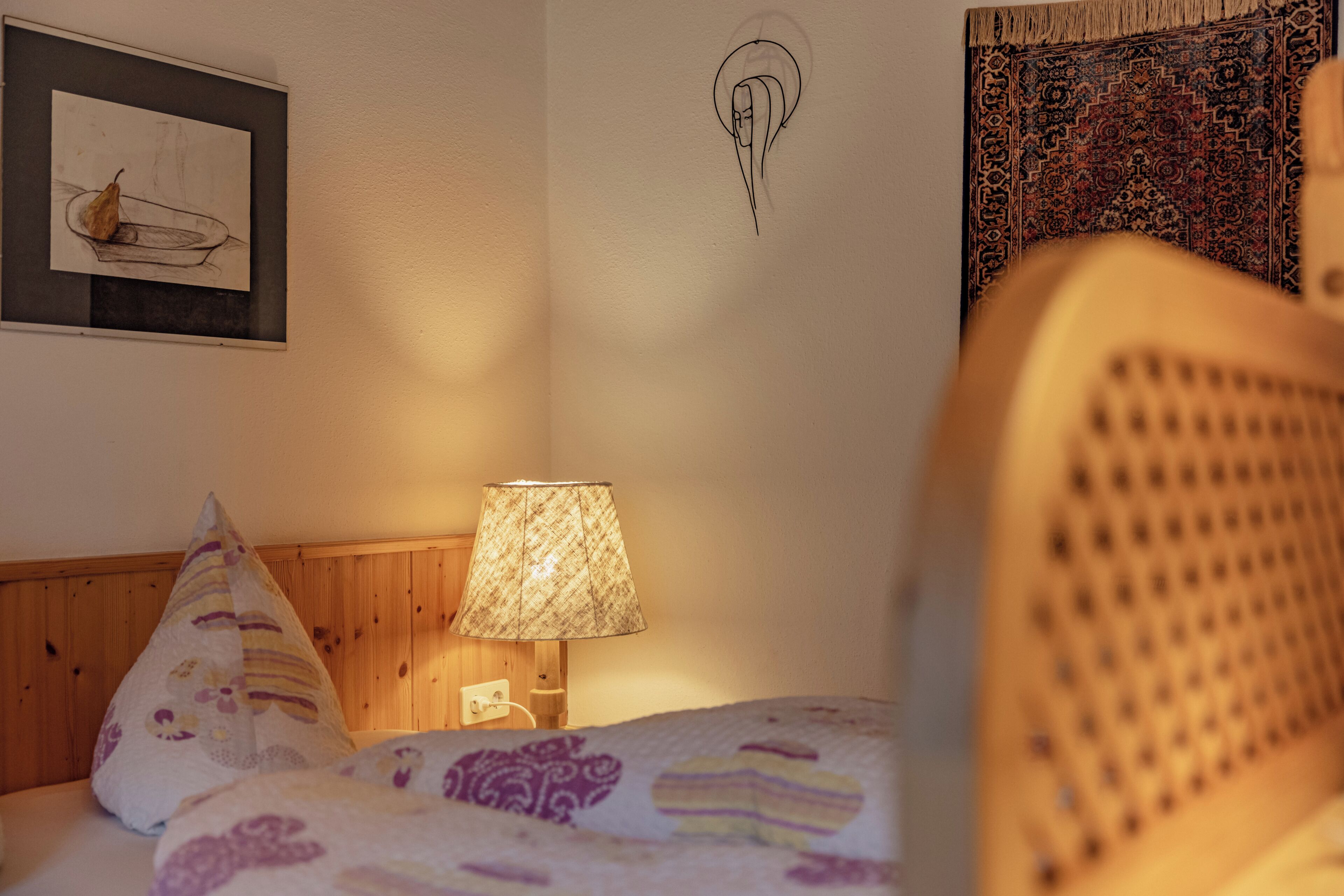 A bedroom with a bed, a lamp, a wall art piece, and a tapestry.