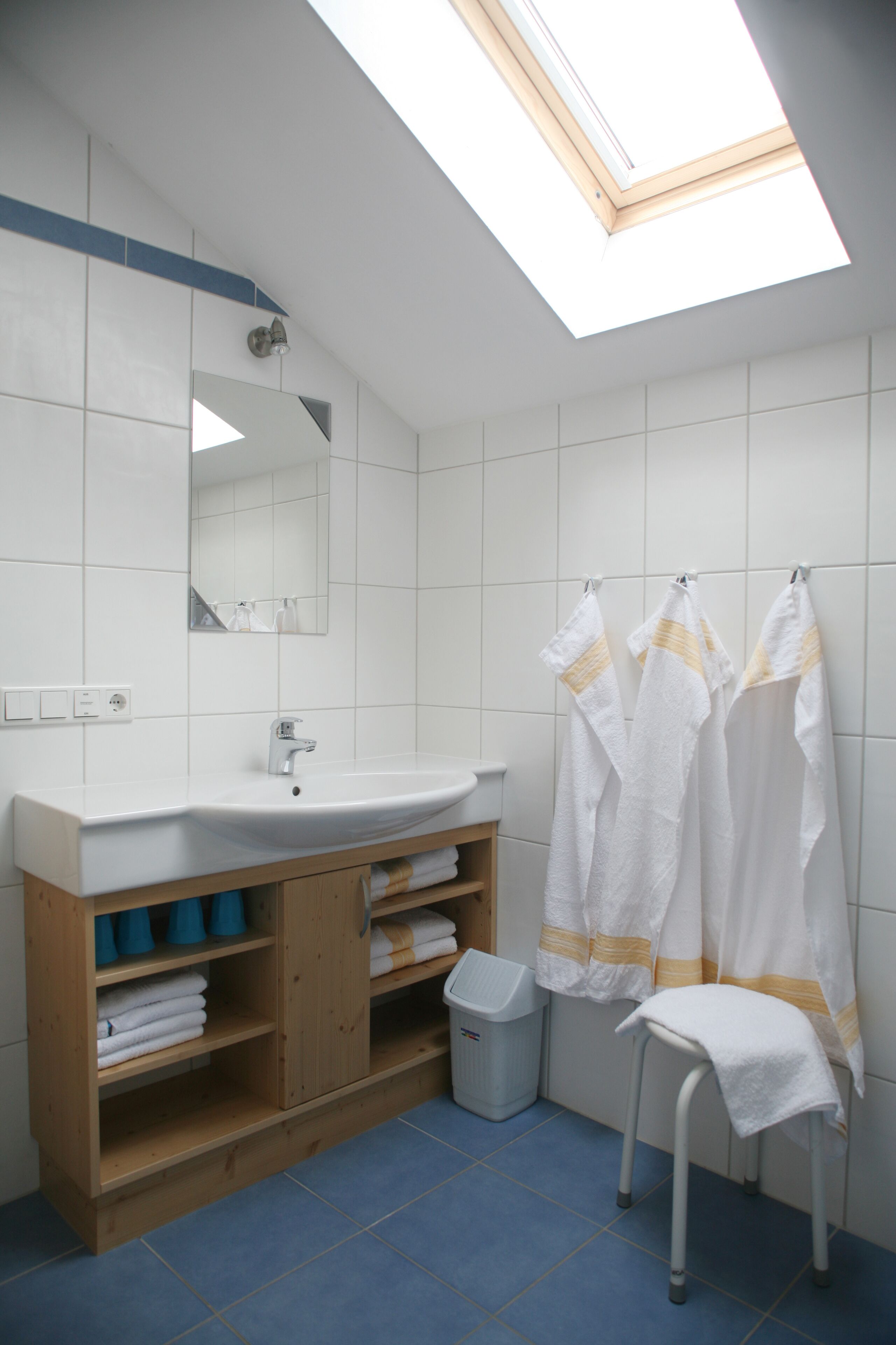 A bathroom with a skylight, white tiles, a wooden vanity, a sink, and two towels hanging on a rack.