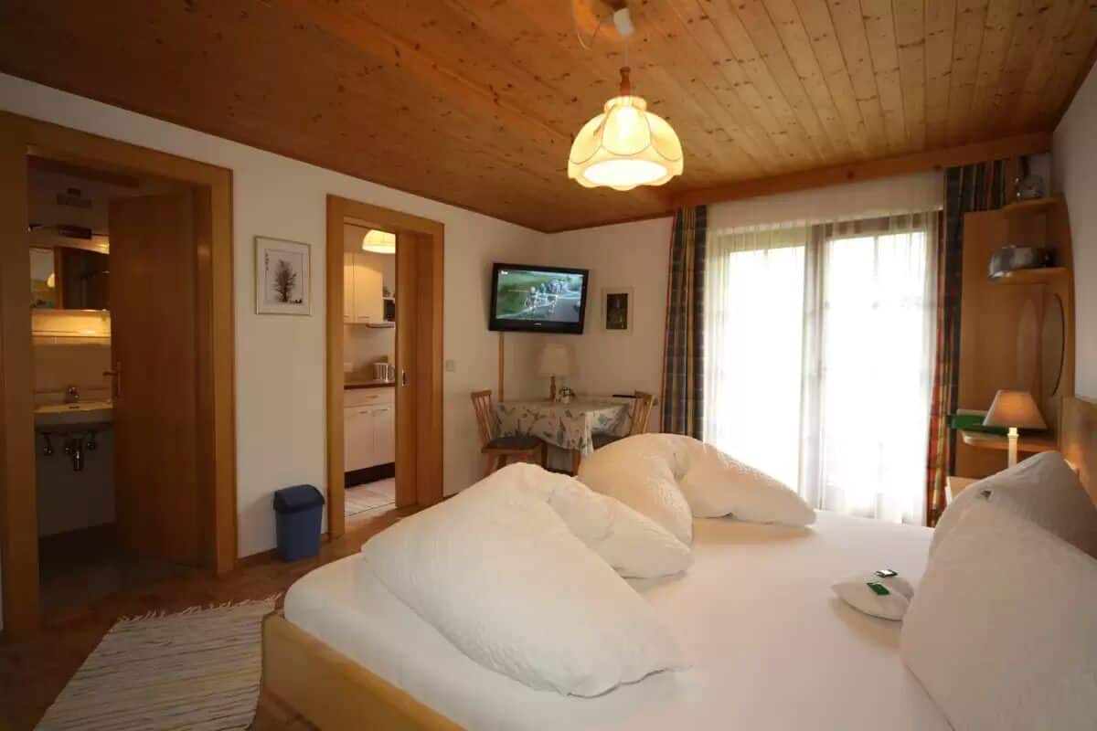 Una habitación de hotel con techo de madera, una cama con ropa de cama blanca, un televisor en la pared y una ventana con cortinas.