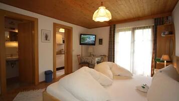 Una habitación de hotel con techo de madera, una cama con ropa de cama blanca, un televisor en la pared y una ventana con cortinas.