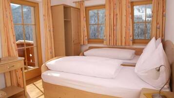 A bedroom with a wooden bed, a bedside table with a lamp, and a window with curtains.
