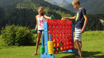 Two children playing with a large, colorful game structure in a grassy field with mountains in the background.