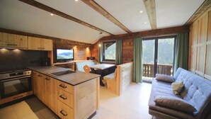 Una habitación acogedora de estilo cabaña, con kitchenette, un sofá y un amplio ventanal con vistas a un balcón.