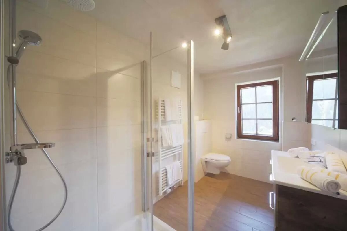 A modern bathroom with a glass shower enclosure, a toilet, and a sink with towels.
