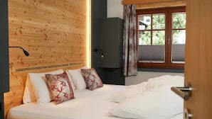 Un dormitorio con cabecera de madera, cama con ropa de cama blanca y almohadas florales rojas, lámpara de noche, armario y ventana con cortinas.