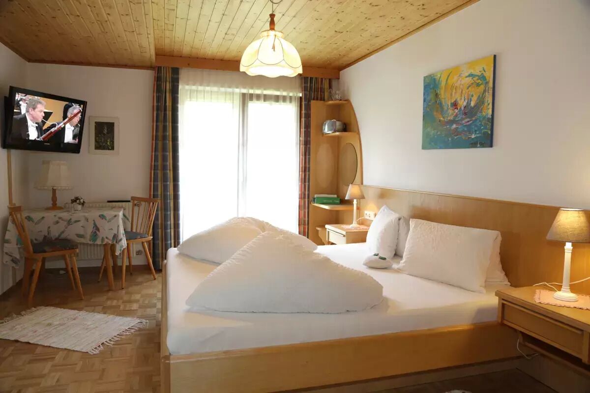 Hotelkamer met een houten plafond, een bed met wit beddengoed, een televisie aan de muur en een schilderij.