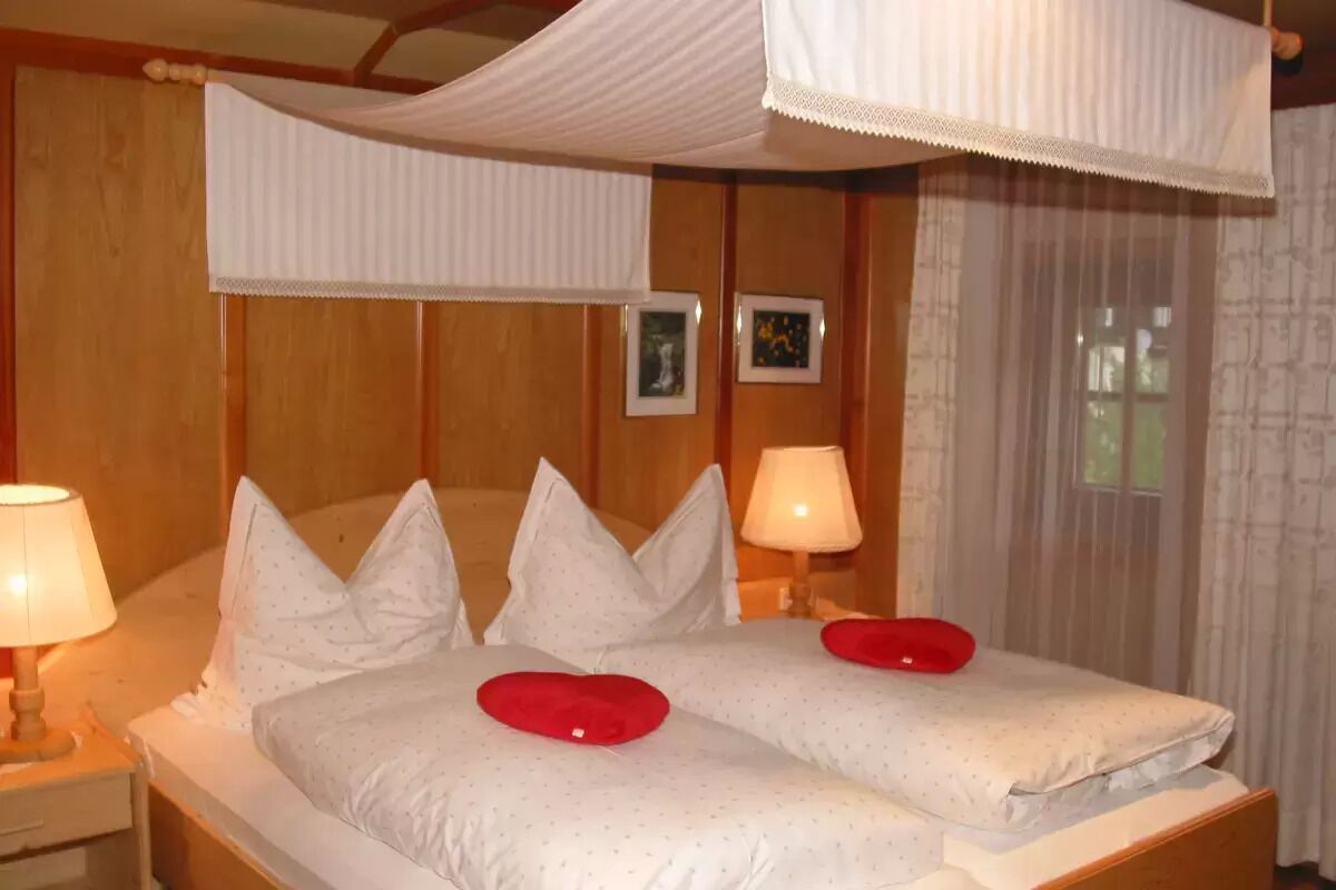 Ein Doppelbett mit weißer Bettwäsche und roten Kissen, zwei Nachttische mit Lampen sowie ein Baldachin darüber.