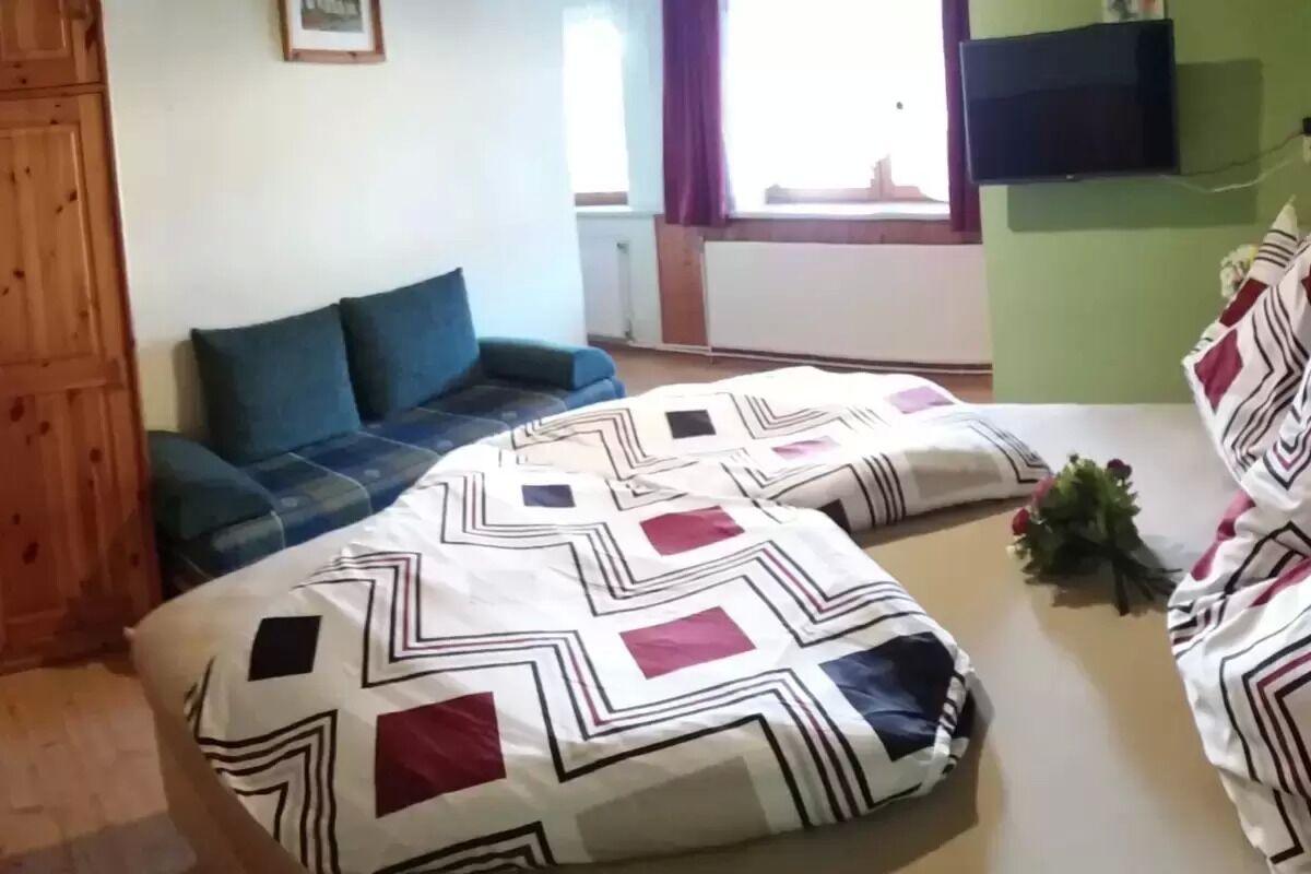A room with a bed, a blue sofa, a TV mounted on the wall, and a window with curtains.