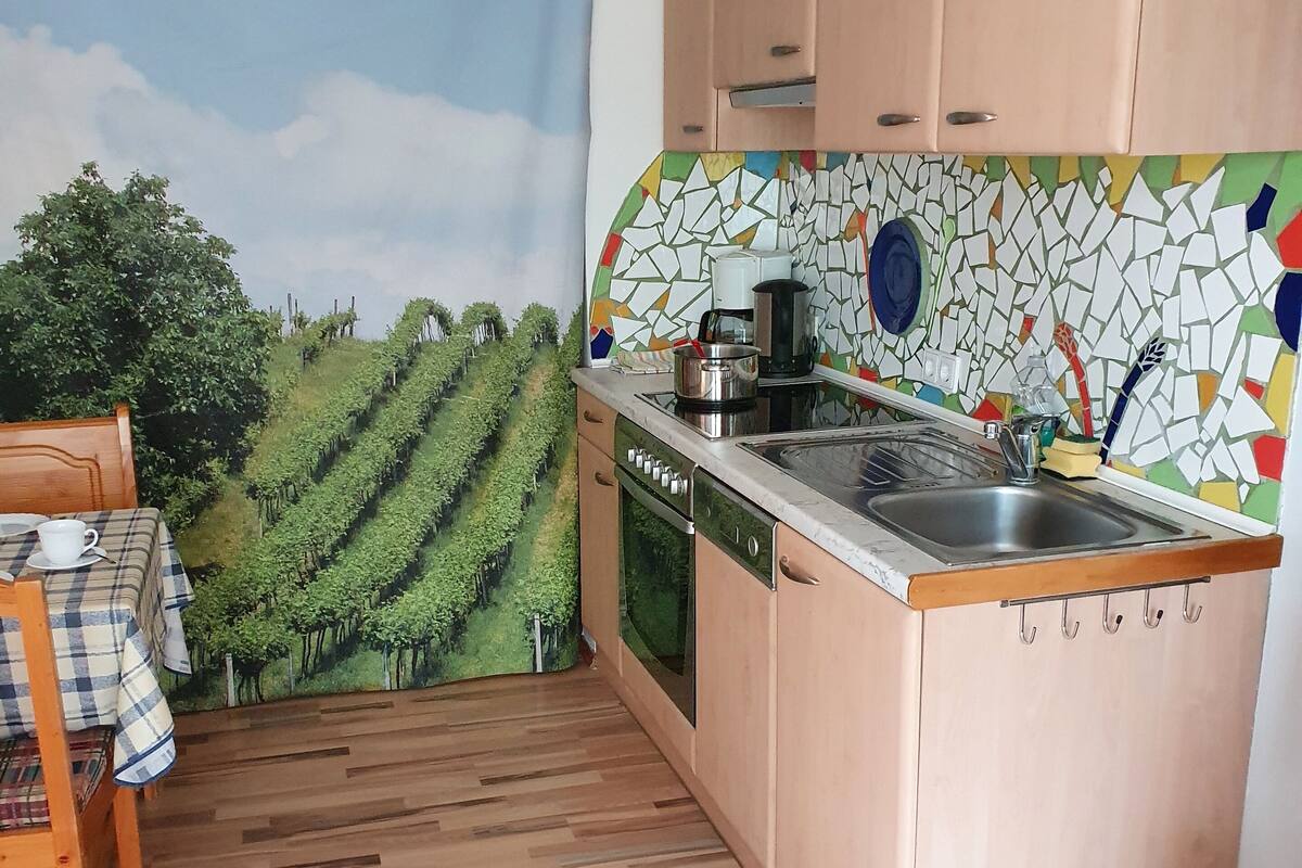 Una cocina con armarios de madera, salpicadero de azulejos y un mural con motivos de viñedos.