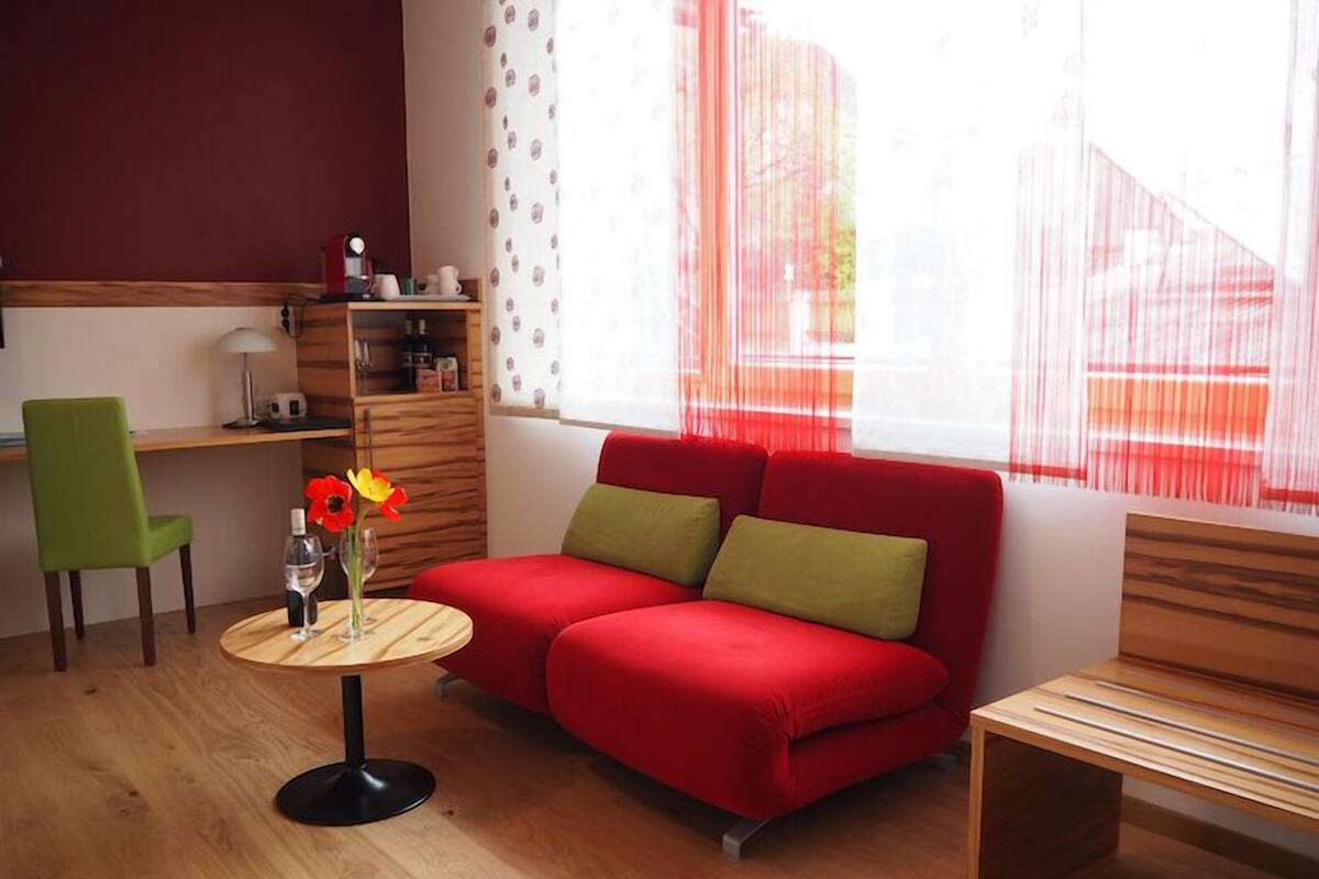 Una sala de estar moderna con un sofá rojo, un sillón verde y una pequeña mesa de madera con un florero.