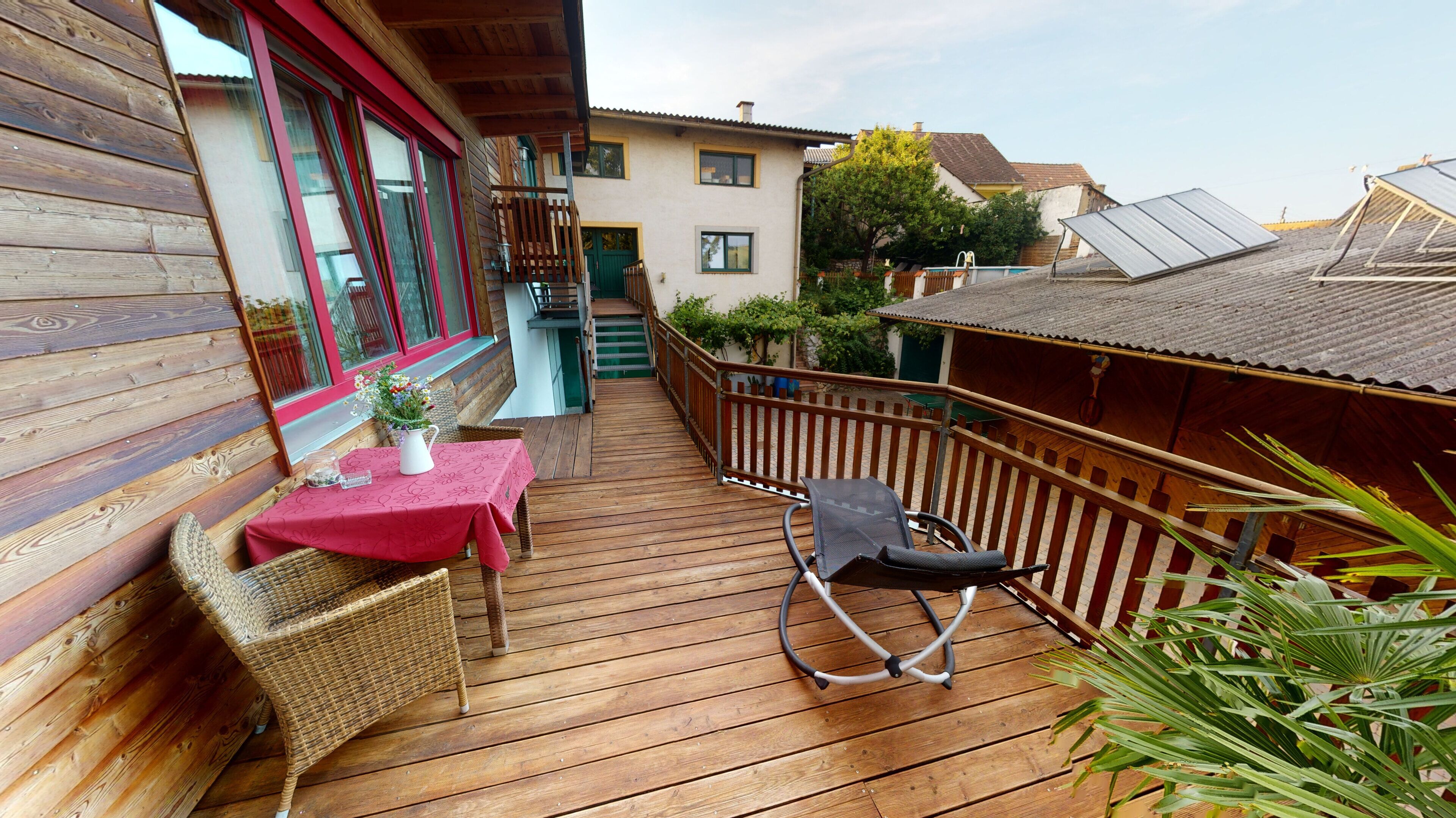 A wooden deck with a table and chairs, a small staircase, and a view of neighboring houses.