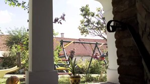 A covered outdoor area with a swing set, a potted plant, and a brick wall. - Weingut Himmelbett (Herrnbaumgarten)