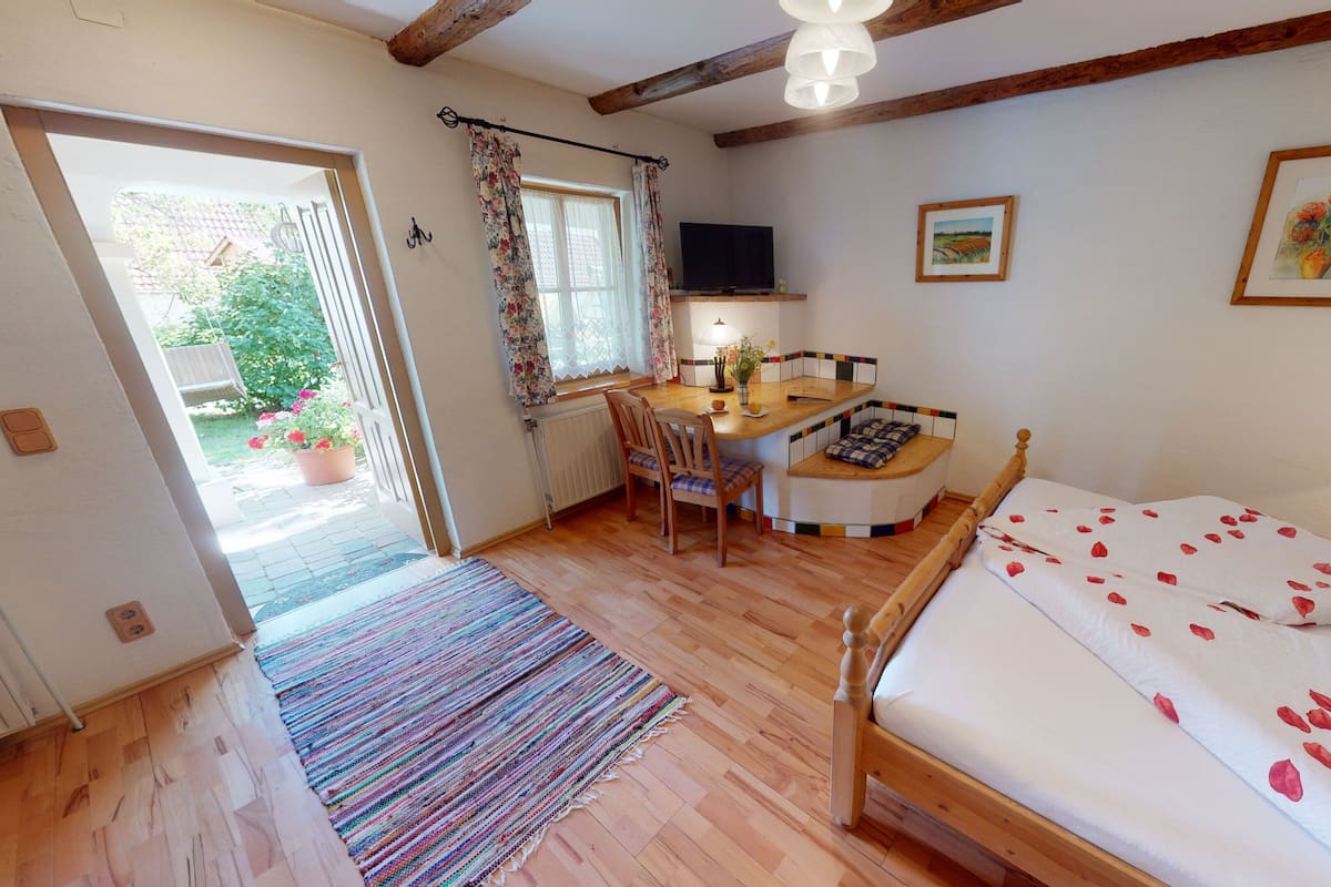 Un dormitorio con una cama de madera, un escritorio con silla, un televisor y una ventana con cortinas florales.