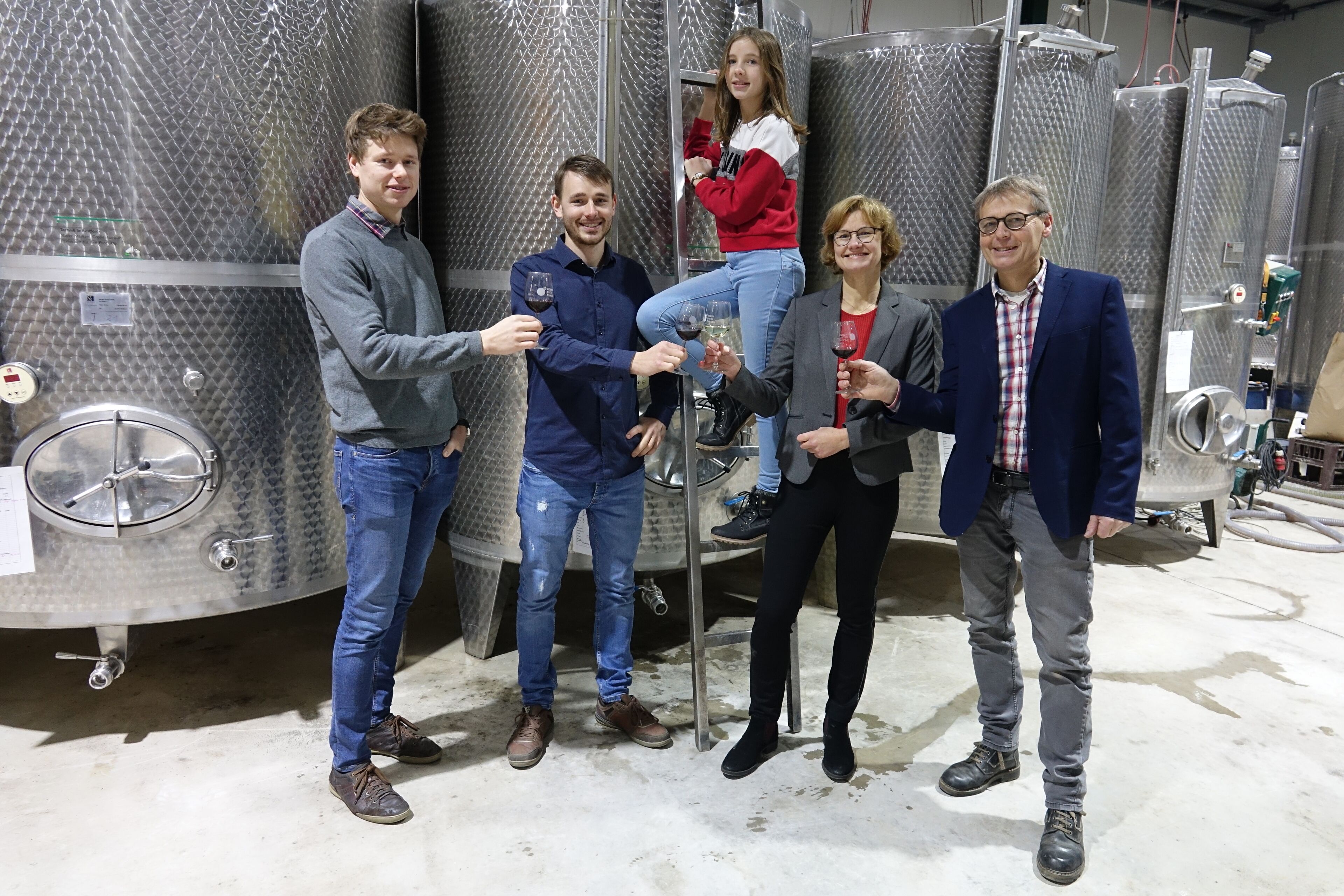 Un grupo de personas de pie en una habitación con tanques metálicos de estilo industrial al fondo.