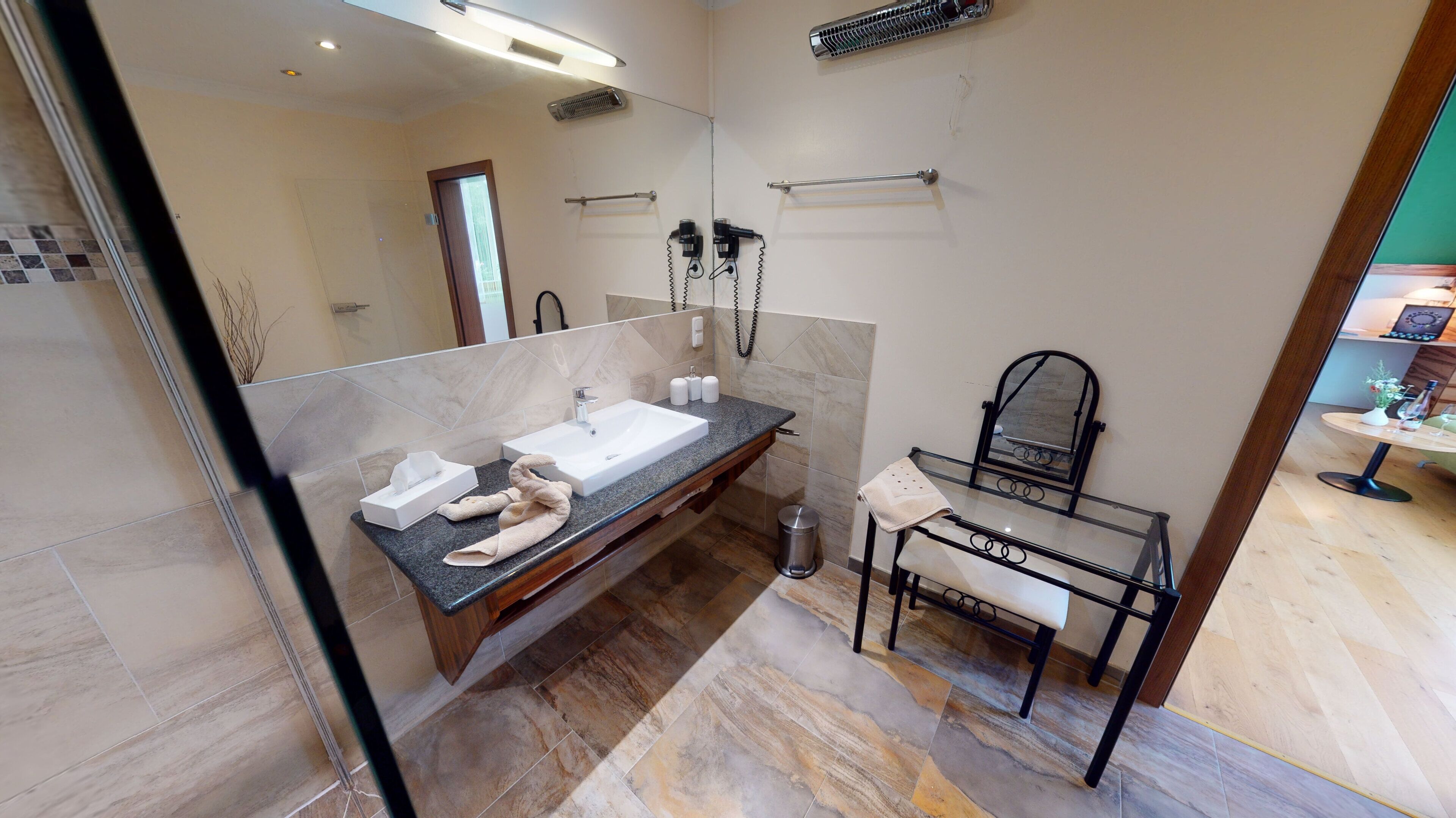 A modern bathroom with a marble vanity, a glass shower enclosure, and a small seating area with a mirror.