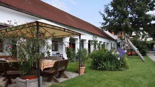 A covered outdoor seating area with wooden furniture and potted plants. - Weingut Himmelbett (Herrnbaumgarten)