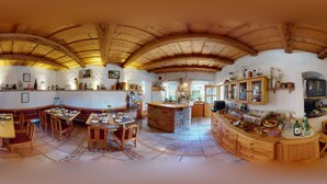 A spacious kitchen with wooden cabinetry, a central island, and a dining area with benches. - Weingut Himmelbett (Herrnbaumgarten)