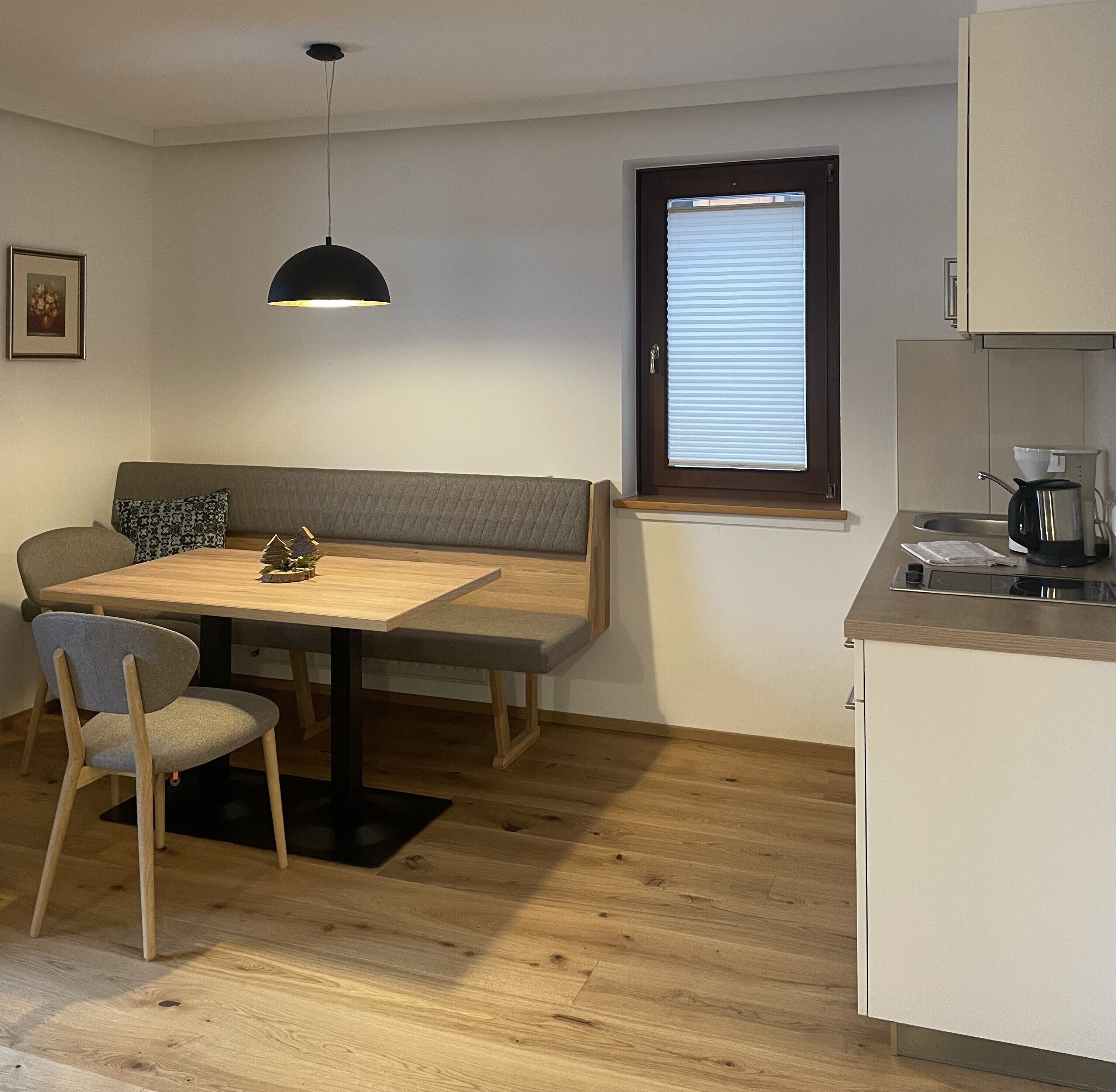 A compact kitchen with a dining area, a bench, and a window with blinds.