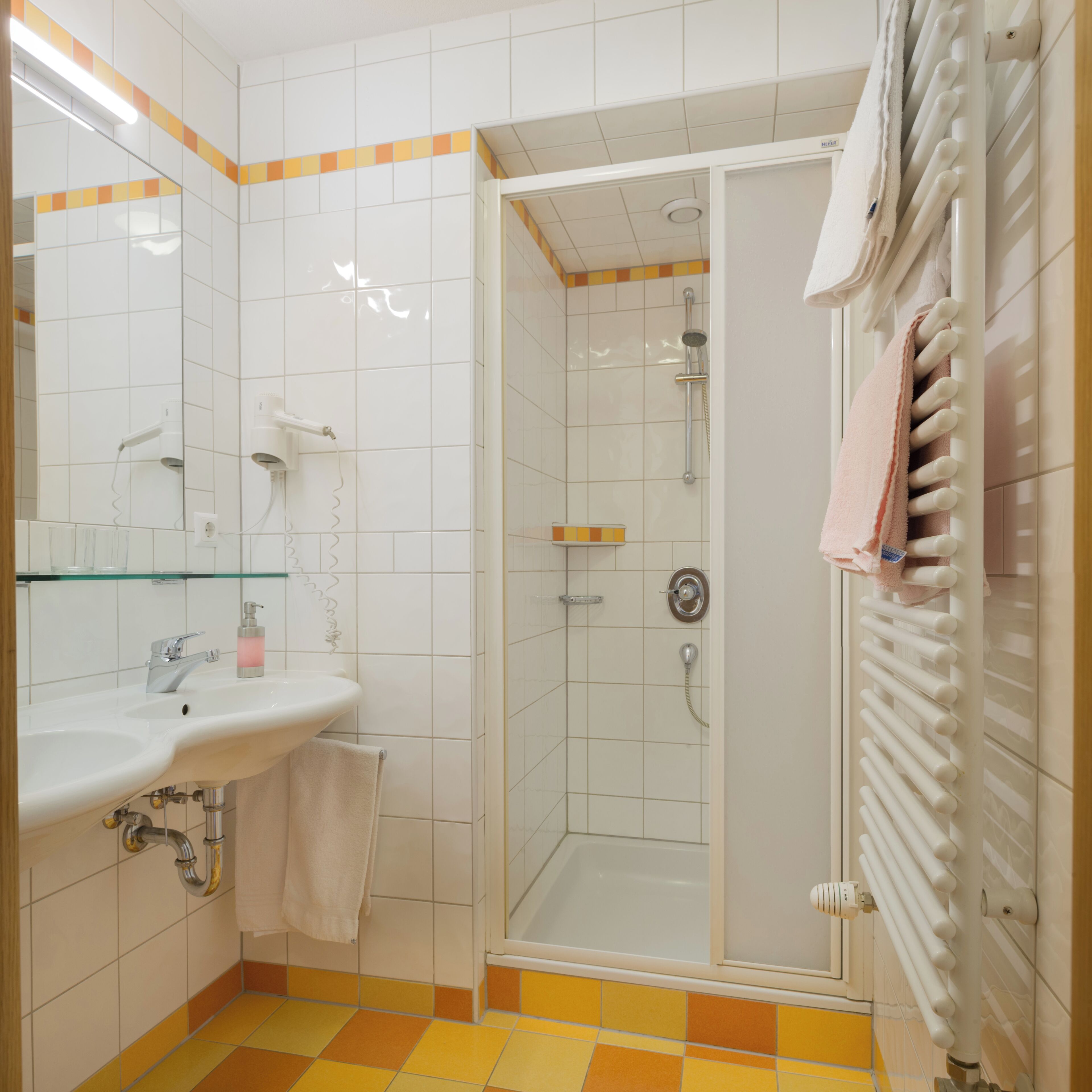 Een badkamer met een douchecabine van glas, een wastafel met spiegel en een handdoekrek.