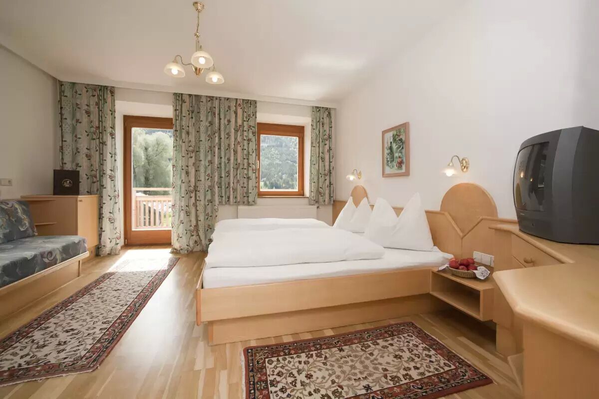A hotel room with a large bed, a sofa, a TV, and a balcony with curtains.