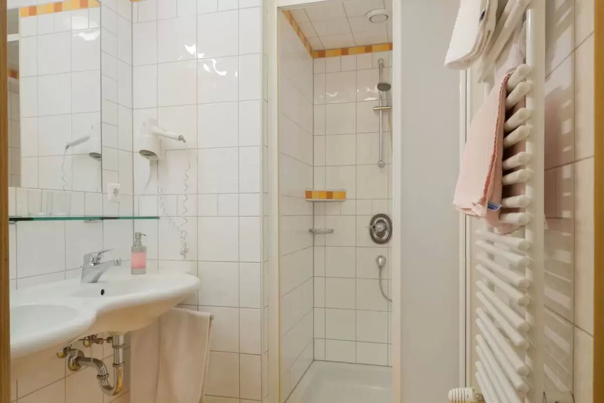 A bathroom with a sink, mirror, shower, and towel rack.