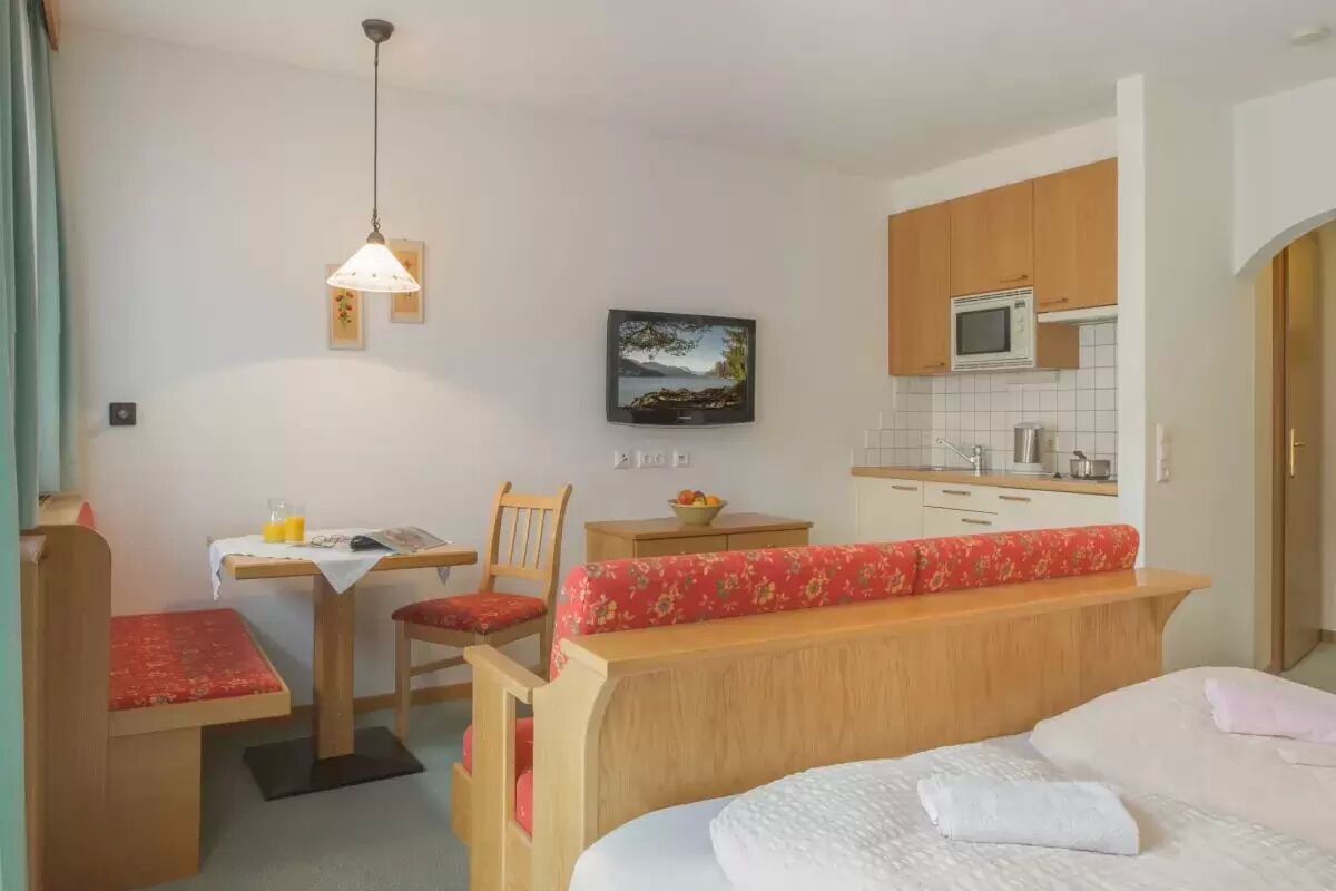 A compact room with a bed, a desk with a chair, a small table with a chair, a microwave, and a sink.