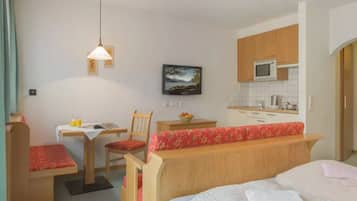 A compact room with a bed, a desk with a chair, a small table with a chair, a microwave, and a sink.