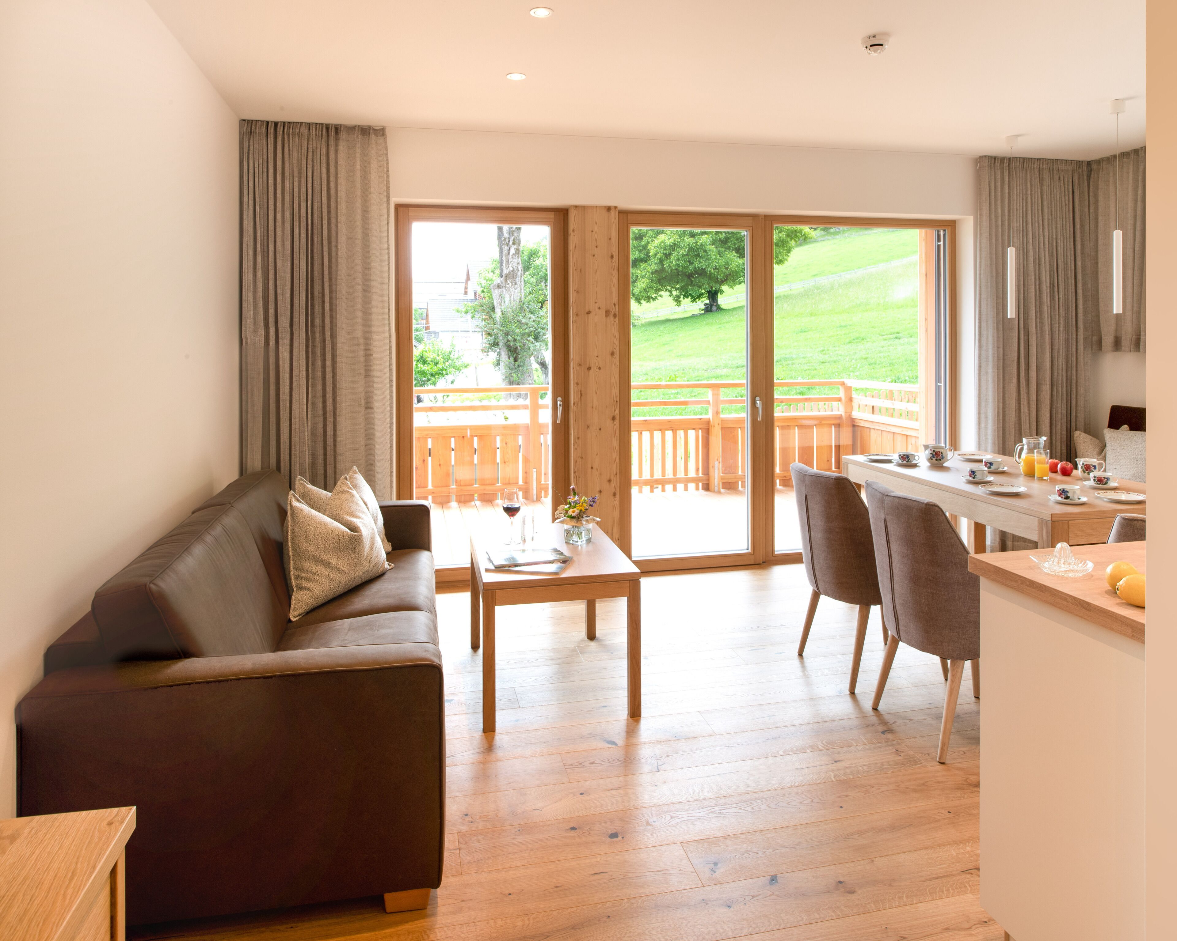 Een moderne woonkamer met een bruine leren bank, een houten salontafel en een eethoek met een houten tafel en stoelen.