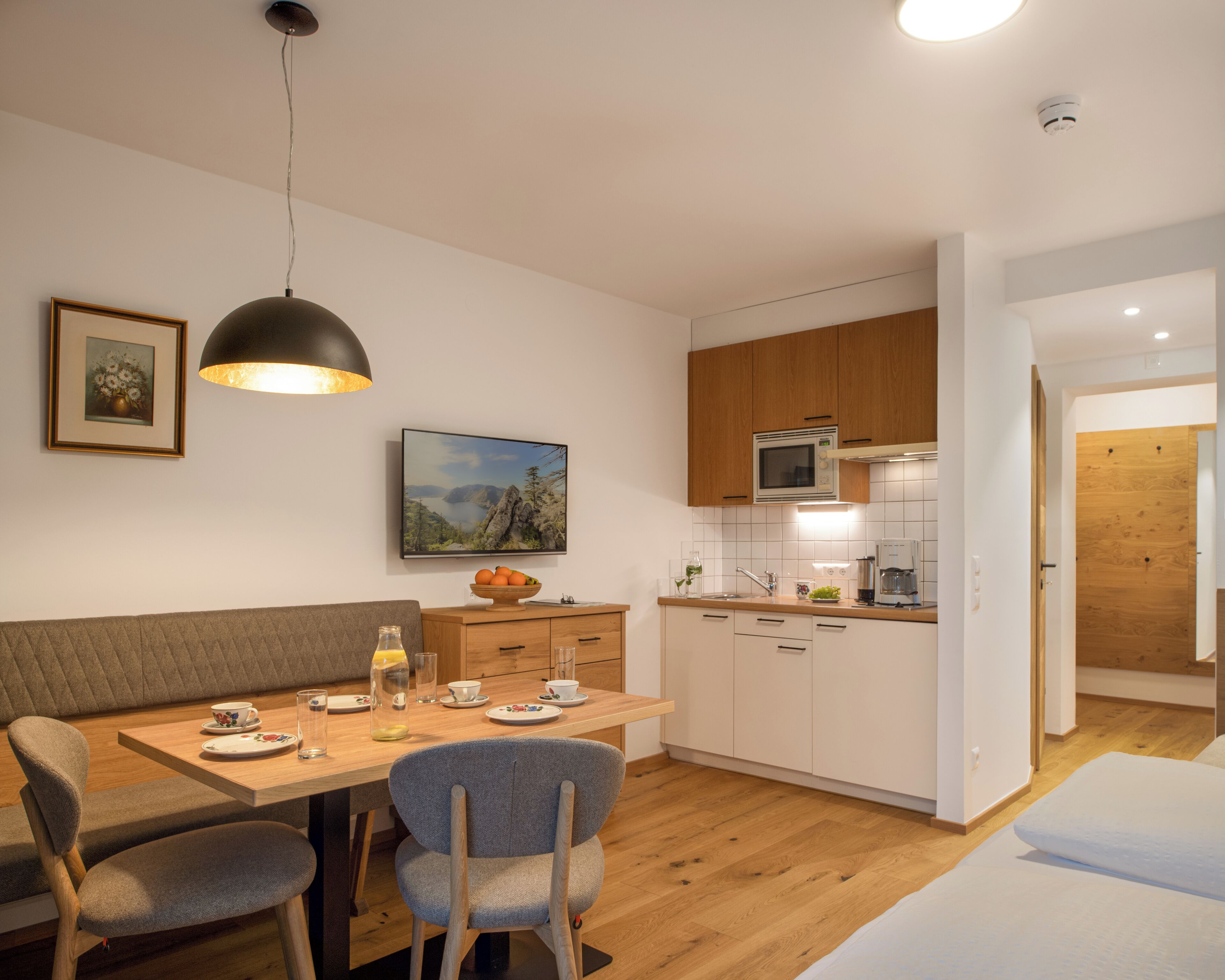 A modern kitchen with wooden cabinets, a dining table with chairs, a painting on the wall, and a ceiling light.