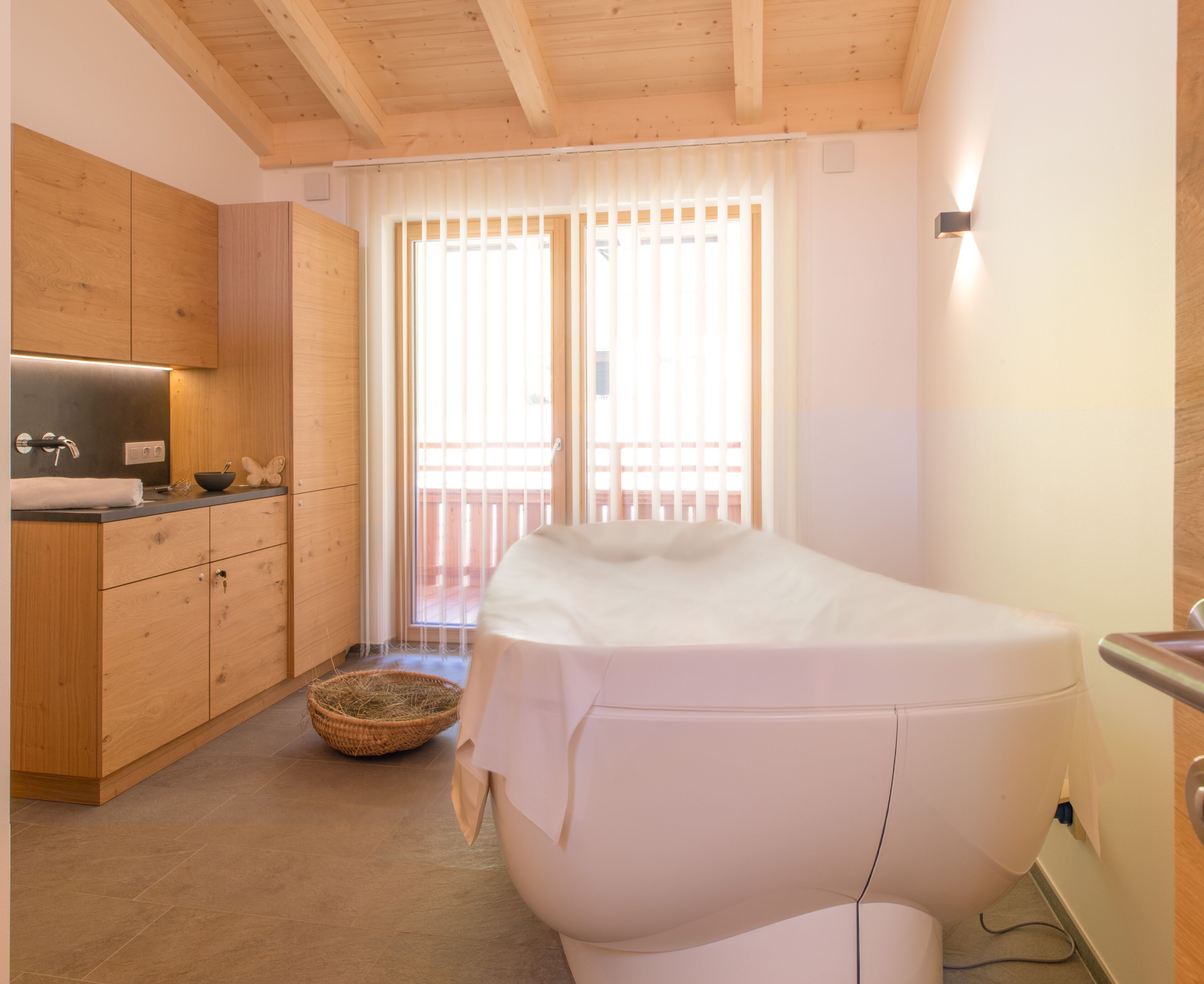 A modern bathroom with a bathtub, wooden cabinets, and a window with blinds.
