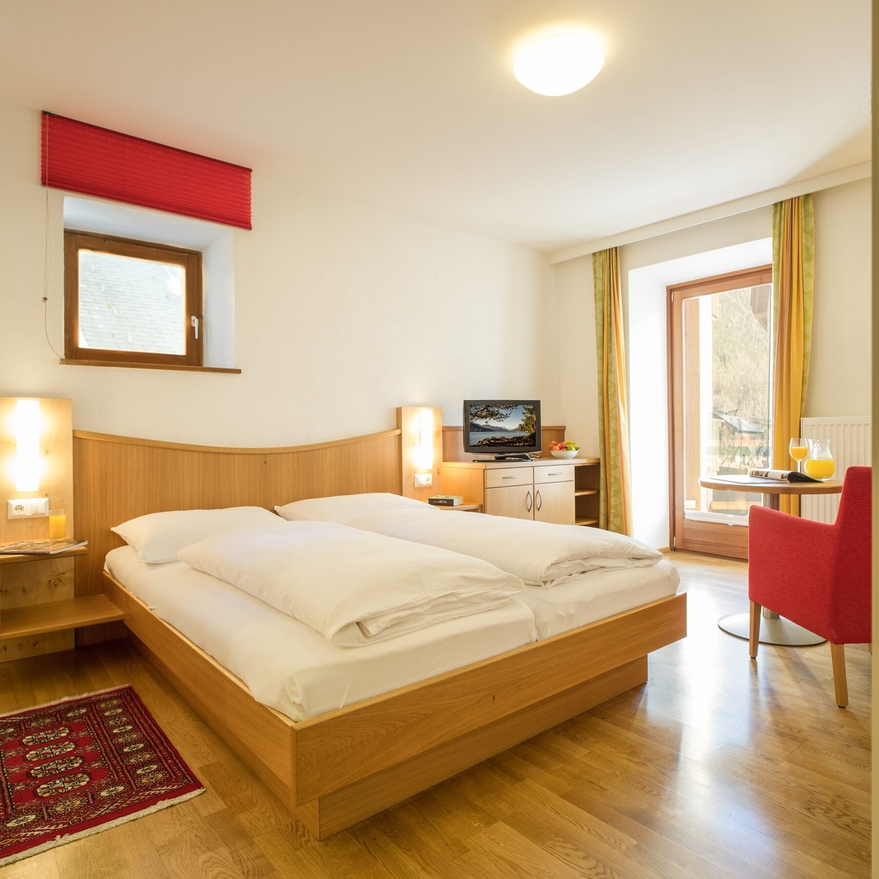 A hotel room with a wooden bed, a television, a desk with a computer, and a red chair.