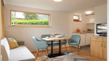 A compact living space with a sofa, a dining table with chairs, a TV, and a kitchen area.