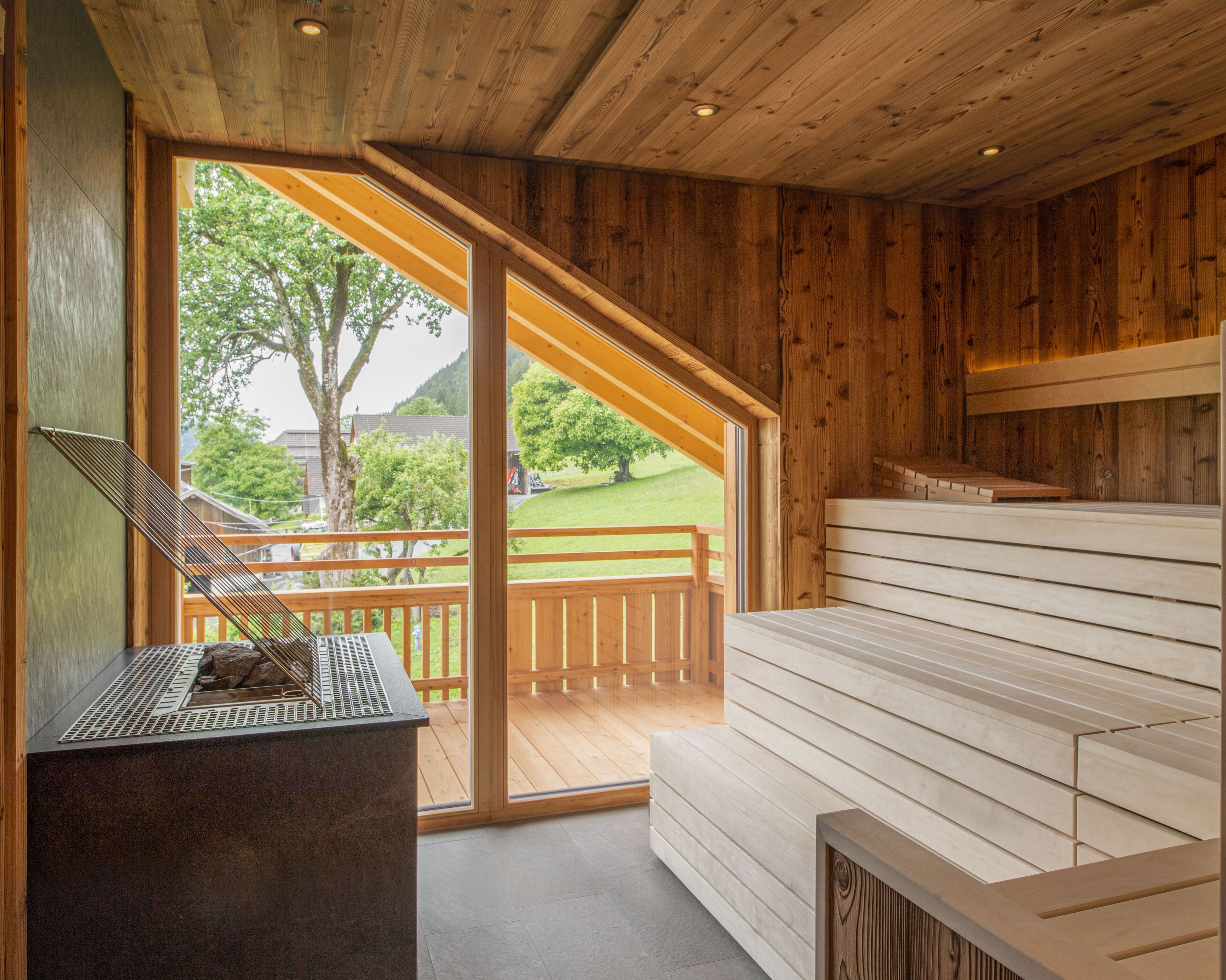 Una sala de sauna con paredes de madera y un banco. Se ve una ventana con vistas a un paisaje verde.