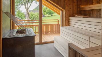 Una sala de sauna con paredes de madera y un banco. Se ve una ventana con vistas a un paisaje verde.