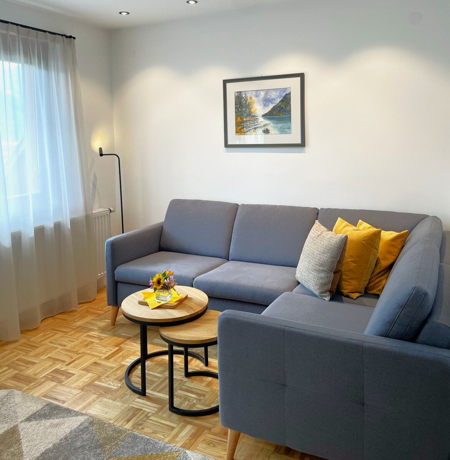 Un soggiorno moderno con un divano grigio, un tavolino rotondo con un vaso di fiori e un quadro appeso al muro.
