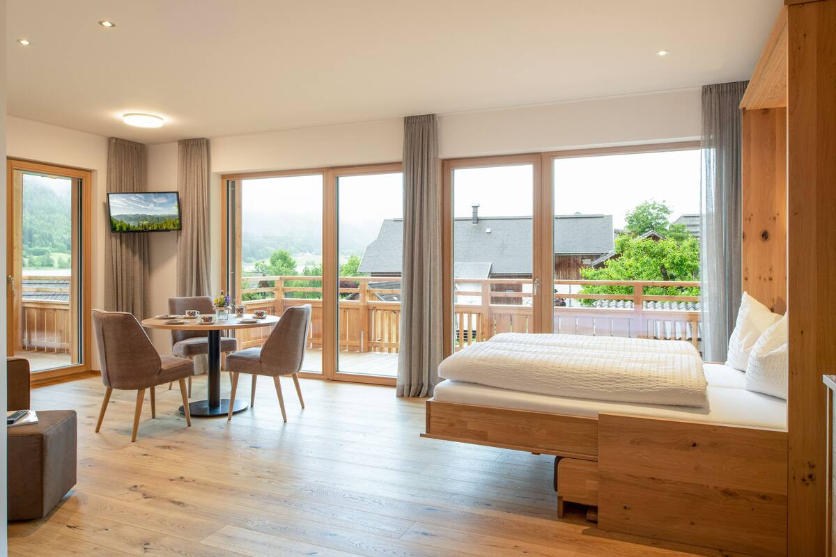 Ein Schlafzimmer mit einem großen Bett, einem Schreibtisch mit Stühlen, einem Fernseher und einem Balkon mit Blick auf die Landschaft.