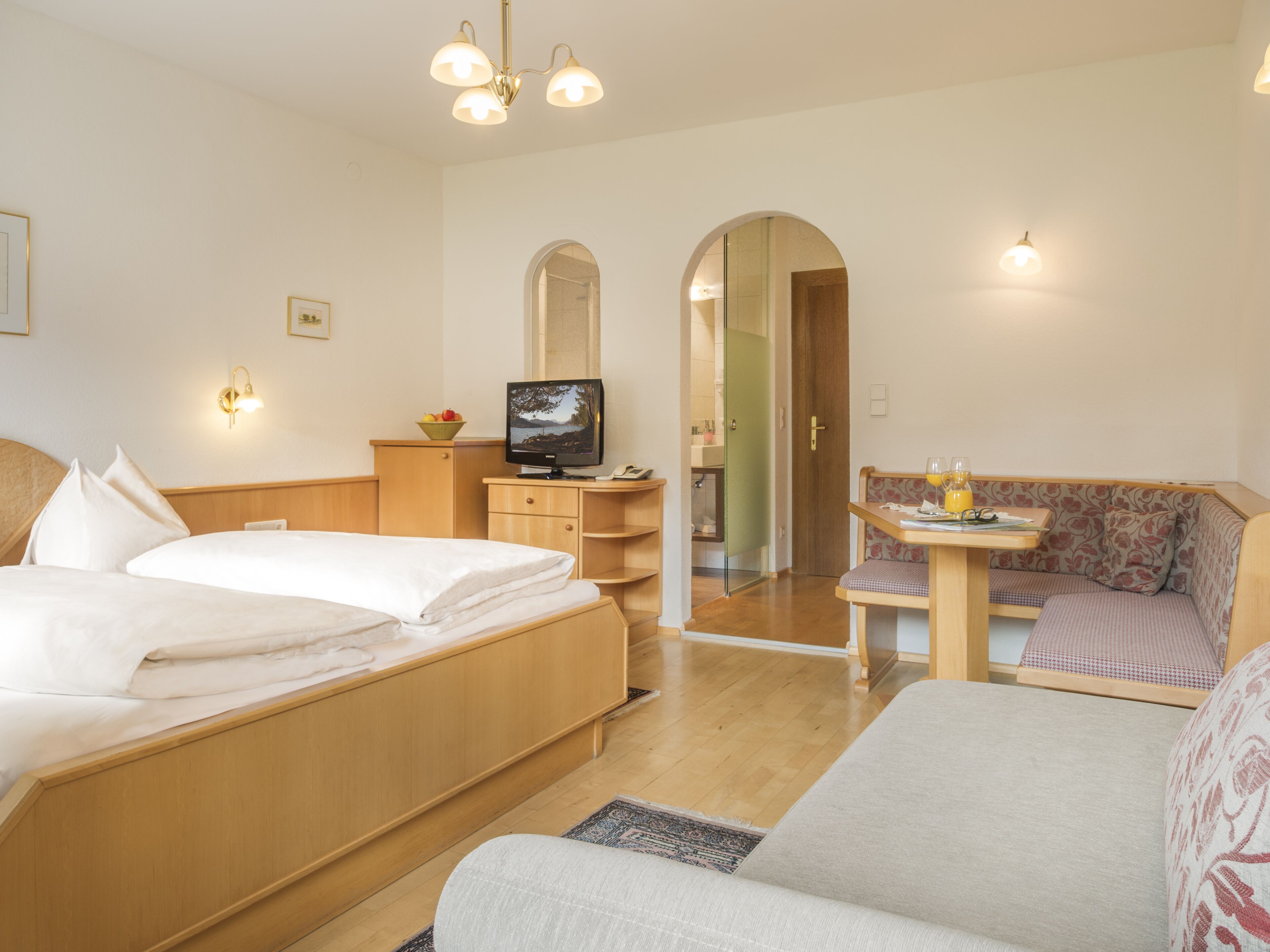 Een hotelkamer met een bed, een bank, een televisie en een klein tafeltje met een glas sinaasappelsap.