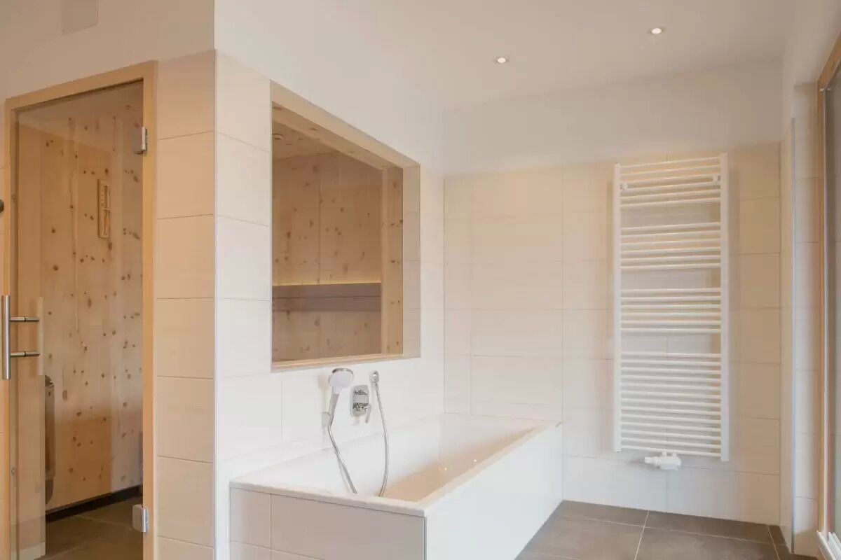 A modern bathroom with a bathtub, a wooden door, and a white towel rack.