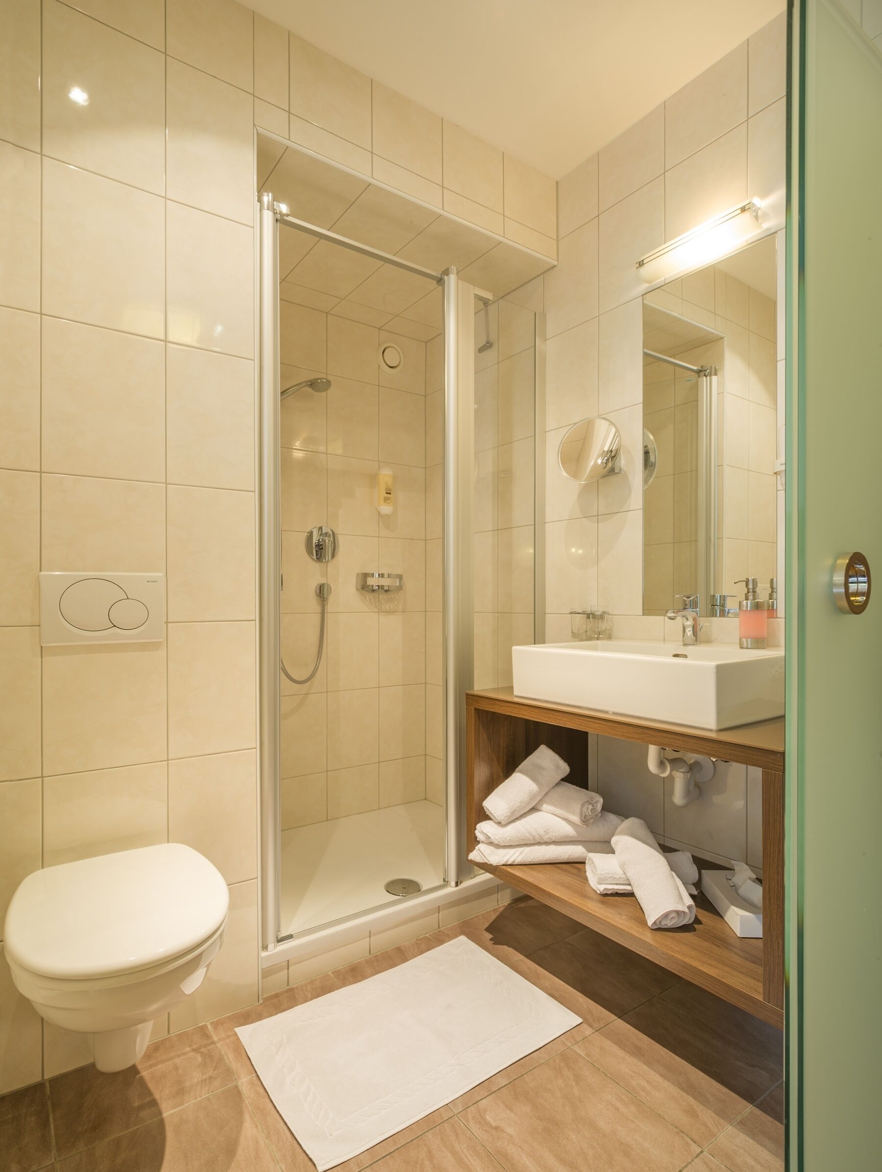 Un bagno moderno con cabina doccia in vetro, lavandino bianco e mobile contenitore in legno.