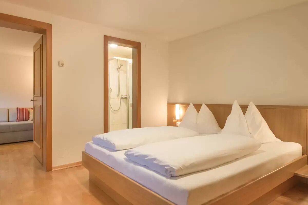 Una camera d'albergo con un letto di legno, lenzuola bianche, una testiera di legno e una porta doccia in vetro.