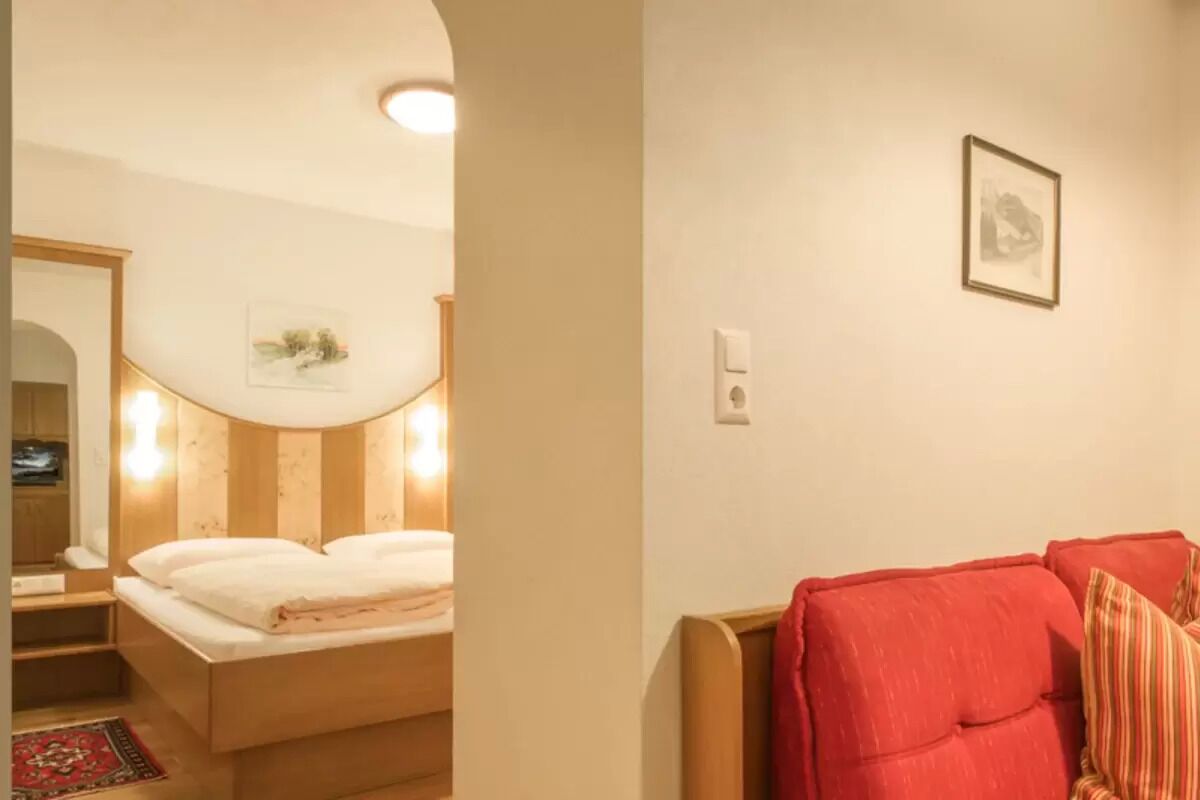 Une chambre à coucher avec un lit, un canapé rouge, un tableau encadré au mur et un miroir.