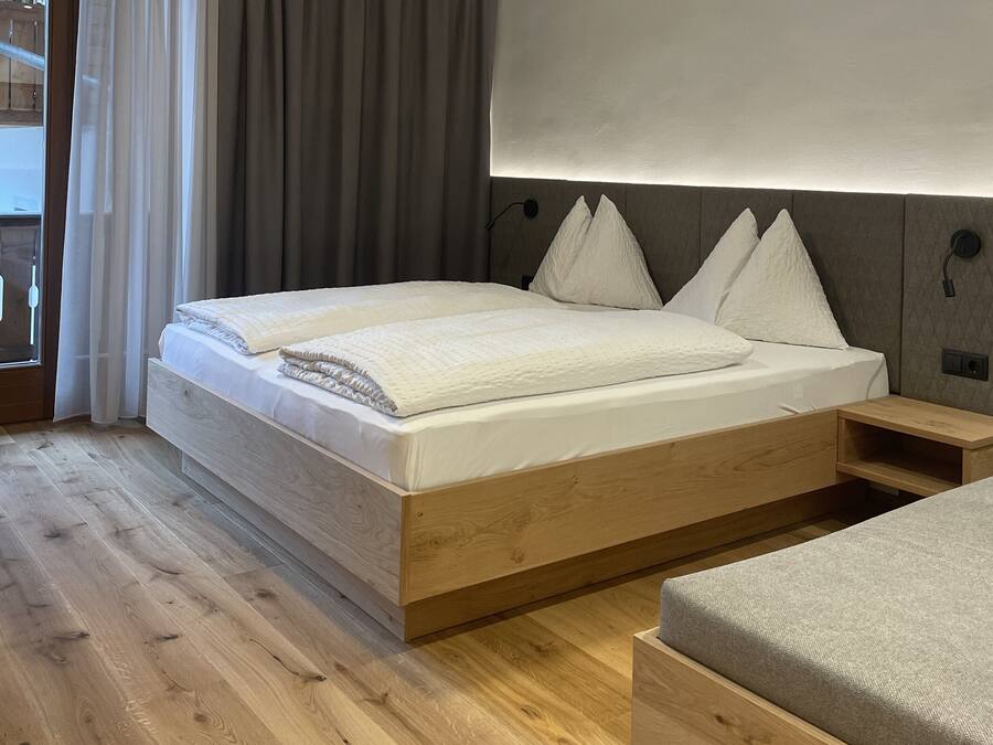 Un dormitorio moderno con un cabecero de madera, un gran ventanal con cortinas y una mesita de noche.