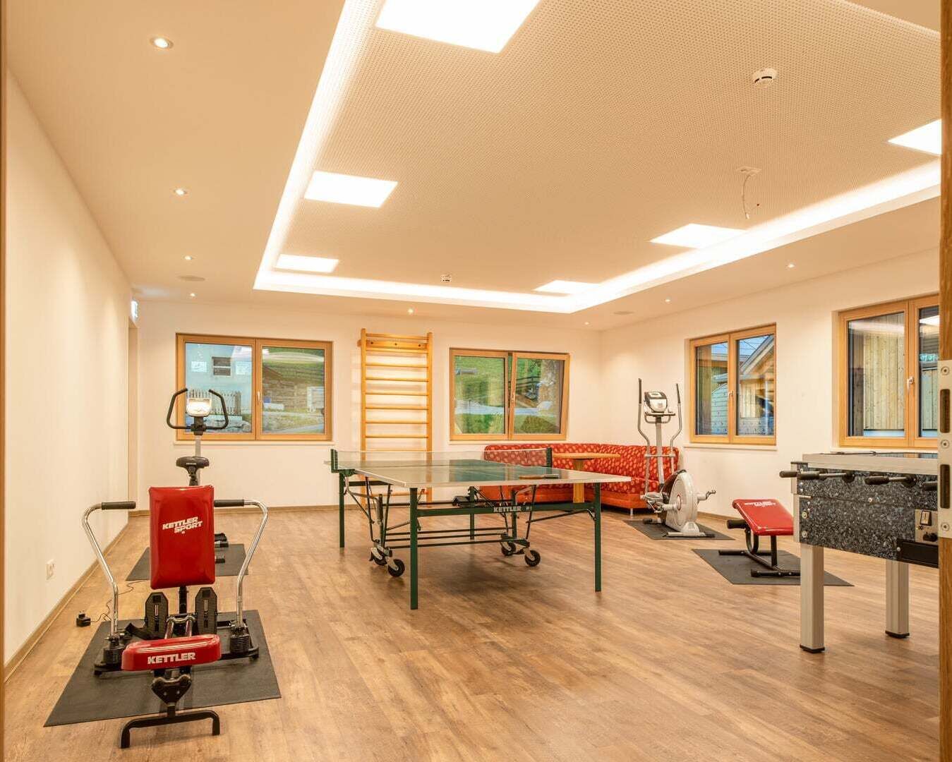 A spacious room with a ping pong table, exercise equipment, and a red sofa.