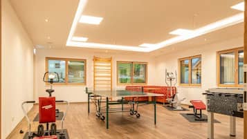 A spacious room with a ping pong table, exercise equipment, and a red sofa.