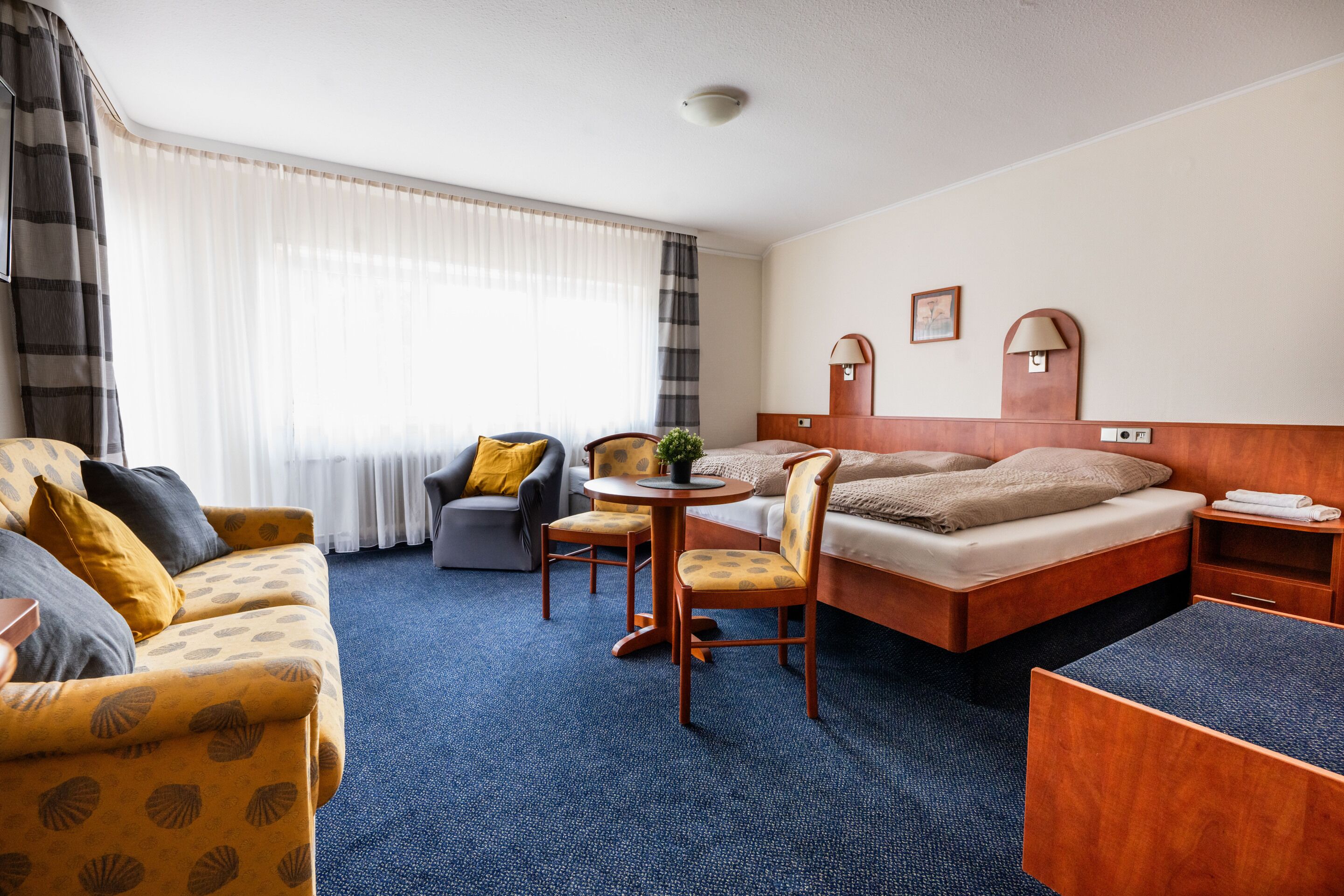 A hotel room with a bed, a sofa, a small table, and a chair.
