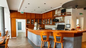 A modern kitchen with wooden cabinets, a central island with stools, and a dining area with a table and chairs. - Landhotel Georgshof (Huenfeld)