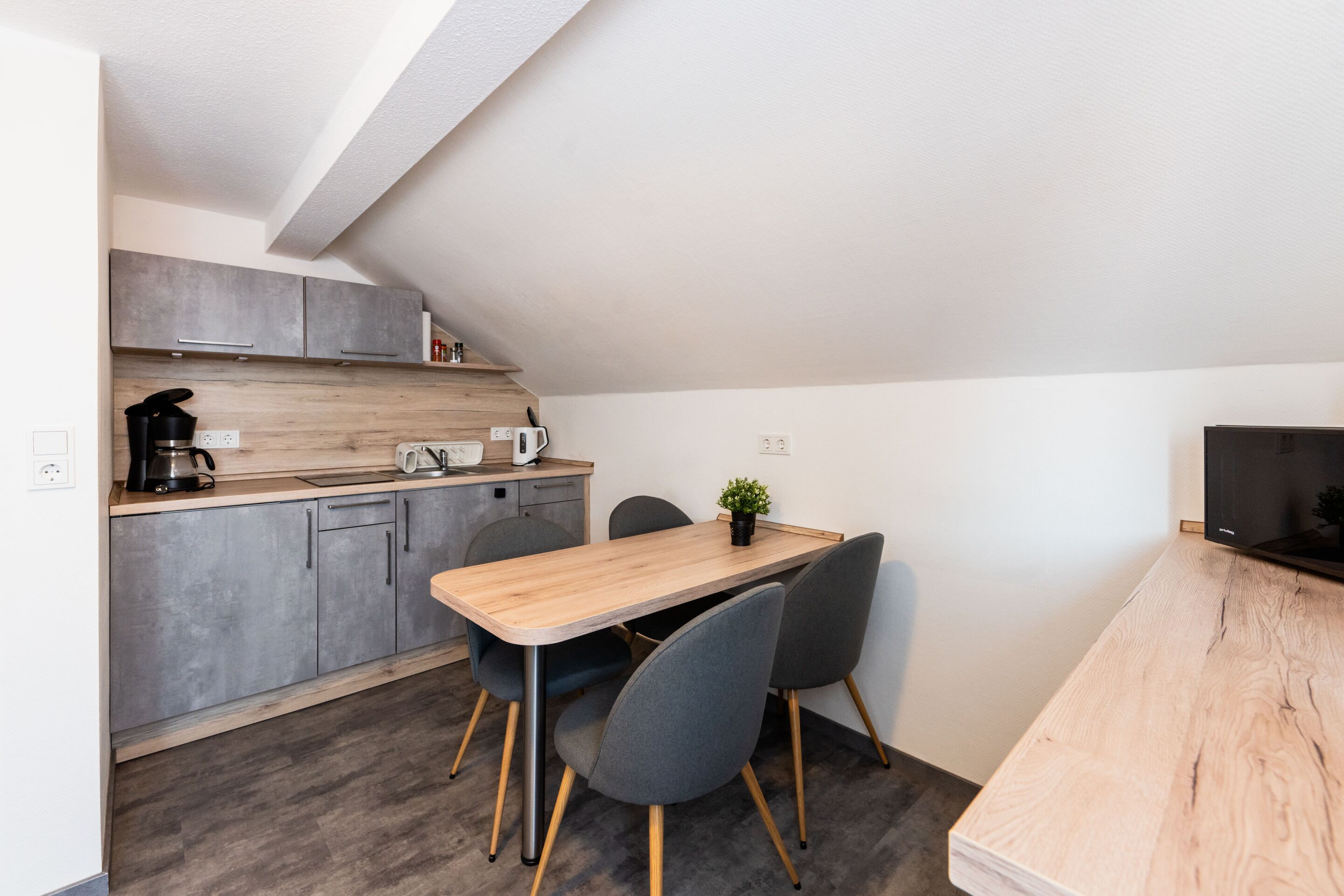 A compact kitchen with a wooden countertop, grey cabinets, and a dining area with a table and chairs.