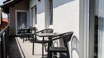 Eine Terrasse im Freien mit Tisch und Stühlen, einem Geländer und einem Gebäude mit Fenstern und einer Tür.