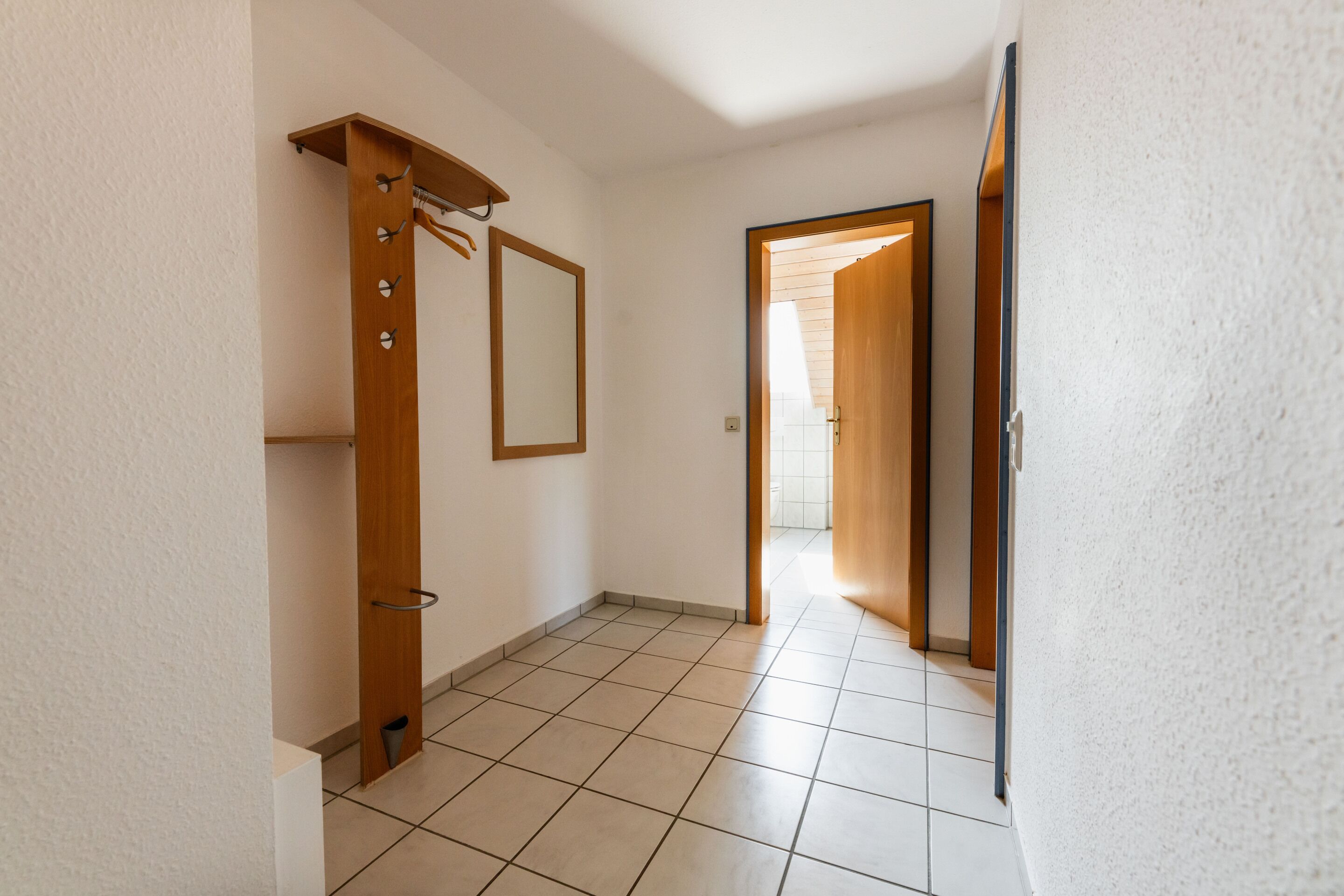A hallway with a wooden coat rack, a mirror, and a door leading to another room.